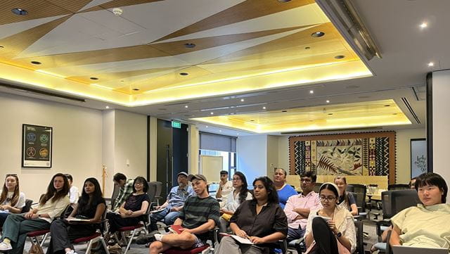 Asian artists sit together, listening intently and looking thoughtful facing the same direction at an information session hosted by Foundation North