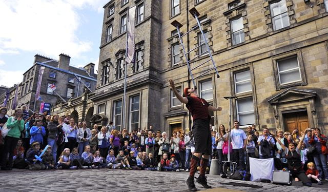 A street performer balances a chair on his chin as an excited crown looks on