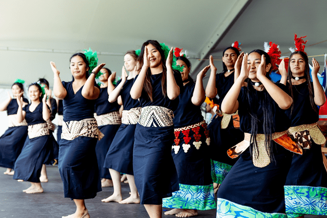 A smiling and singing group of young people perform a traditional Tongan dance, in traditional Tongan dress