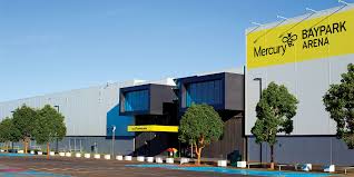 The black and grey Mercury Baypark Arena building entrance, it shows the car park leading to the main building entrance through glass doors.