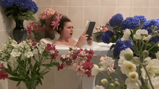 woman reading in the bath surrounded by many vases of flowers